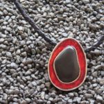 ovaler Anhänger mit schwarzem Flusskiesel, mit rotem Transparentemaille umsäumt